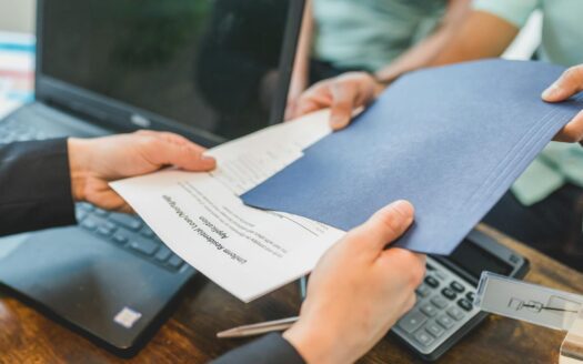 Close-up of hands exchanging real estate documents in an office setting.