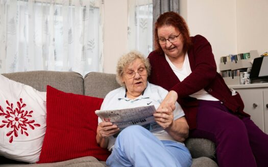 a woman sitting on a couch next to a woman reading a newspaper